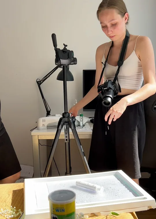 The Éclarén shoot: Viktoryia setting the product in a tray of water on a bed, the camera on its strap and a desk lamp behind her