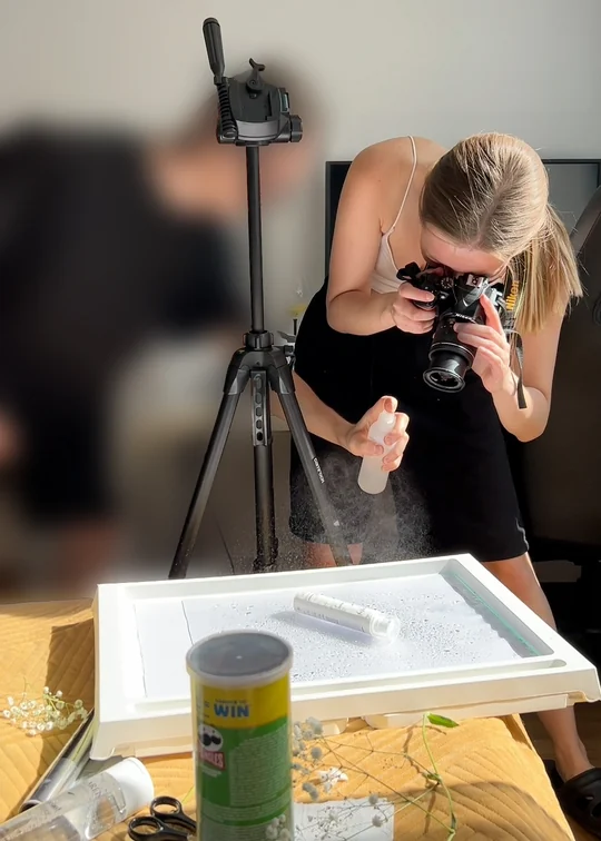 The Éclarén shoot: Viktoryia over the tray of water with the camera to her eye, misting the set with a spray bottle in her free hand